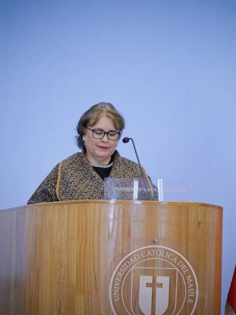 Una mujer está hablando desde un podio en una institución educativa con una bandera chilena al lado.