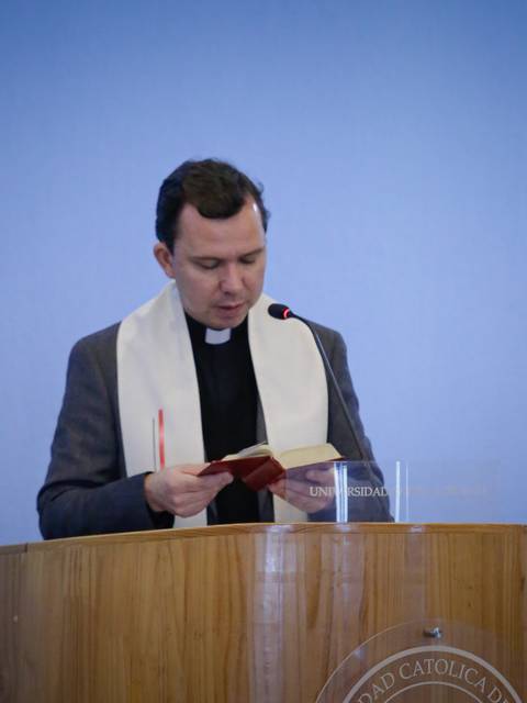 Un sacerdote leyendo un libro frente a un micrófono en un evento formal.