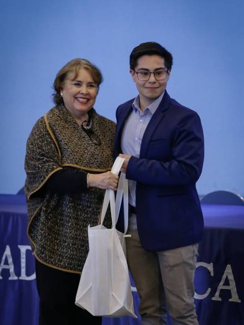 Una mujer y un hombre posan sonrientes mientras sostienen una bolsa en un evento formal.