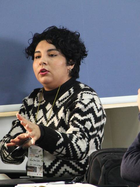 Una mujer con un suéter de diseño geométrico habla apasionadamente en una reunión.