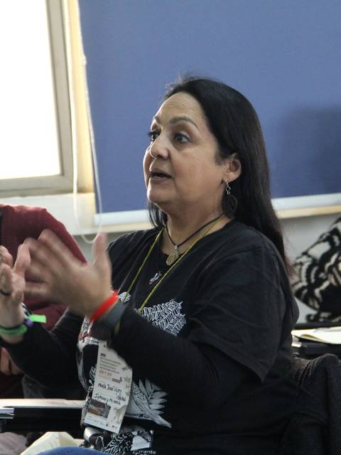 Una mujer habla apasionadamente frente a un grupo de personas en un aula.