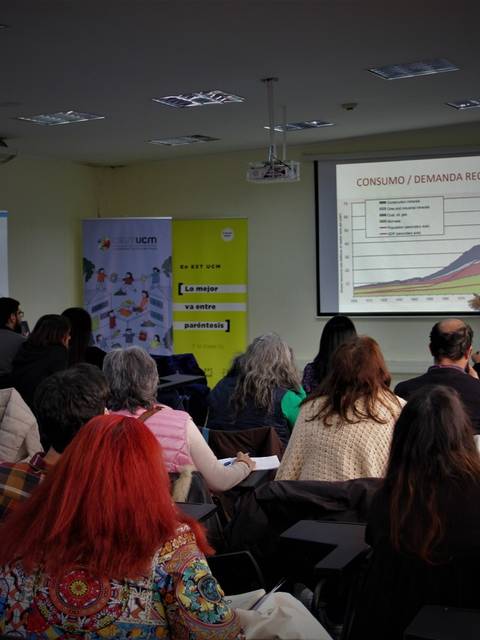 Un grupo de personas asiste a una conferencia mientras un orador presenta un gráfico en una pantalla.