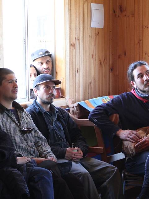 Un grupo de personas sentadas en una sala con paredes de madera, escuchando atentamente.