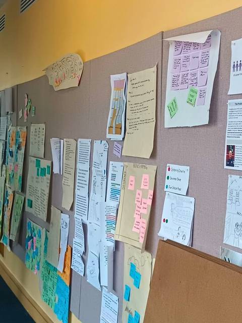 Una persona observa una pared de exhibición llena de diversos documentos y gráficos en un espacio interior.