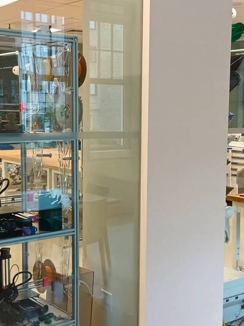 La imagen muestra un espacio moderno con una vitrina que exhibe tecnología y un área de trabajo con computadoras y equipos.