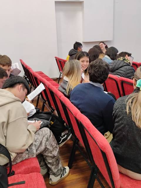 Un grupo de jóvenes sentados en un auditorio, leyendo y conversando entre ellos.
