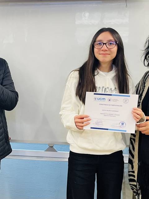 Una joven sostiene un certificado mientras sonríe, rodeada de personas que la aplauden.