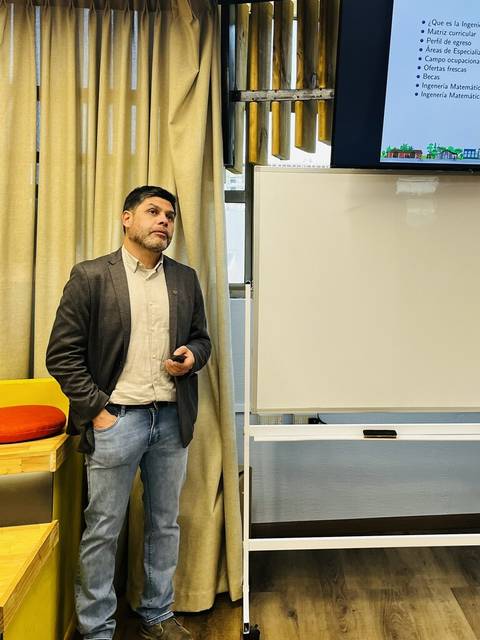 Una persona está presentando un tema en una sala equipada con una pantalla y una pizarra blanca.