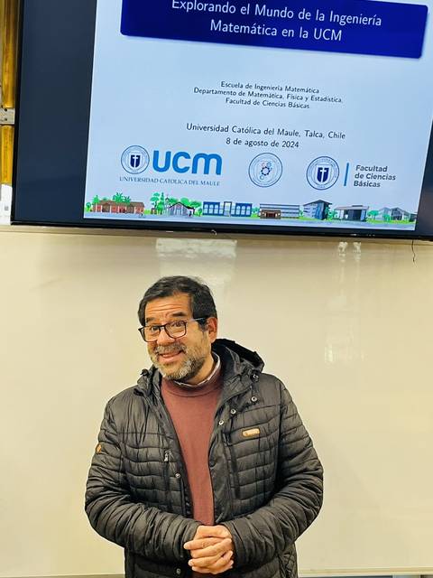 Un hombre sonriente se encuentra frente a una presentación sobre la ingeniería matemática en la UCM.