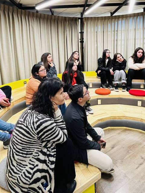 Un grupo de personas sentadas en un espacio moderno, escuchando atentamente.