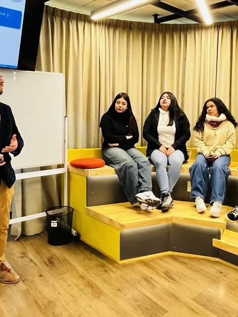 Un hombre habla frente a un grupo de estudiantes en un aula moderna.