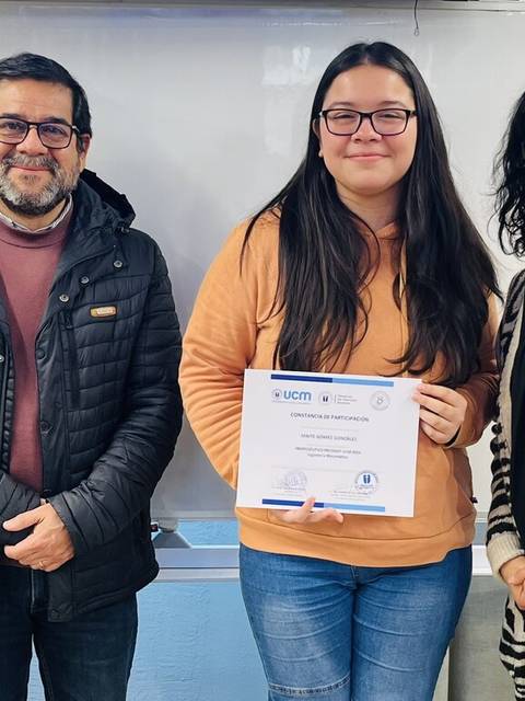 Un grupo de personas celebra la entrega de un certificado a una joven en un entorno educativo.