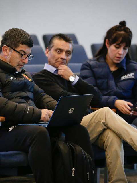 Un grupo de tres personas sentadas en un auditorio, dos de ellas utilizando dispositivos electrónicos.