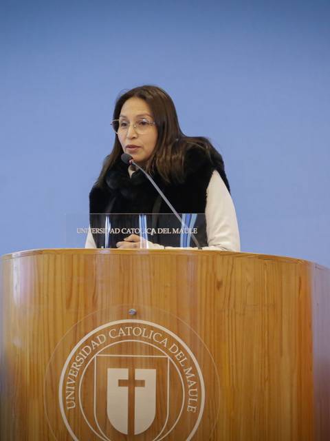 Una mujer está hablando detrás de un podio en un evento académico en la Universidad Católica del Maule.