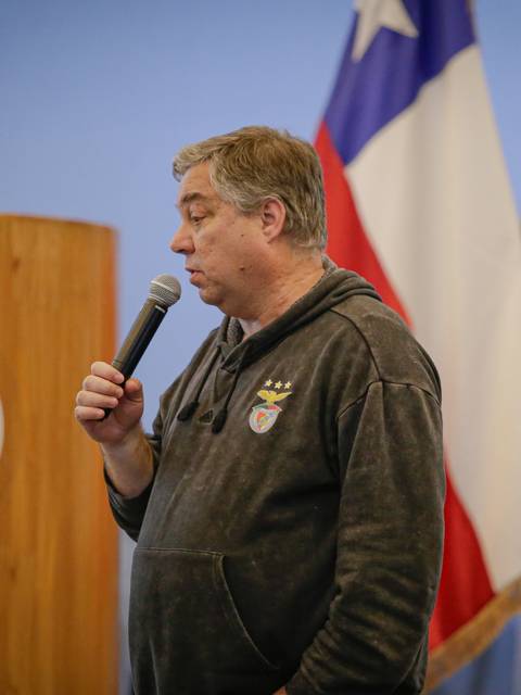 Una persona está hablando en un evento en un auditorio con banderas y un podio visible al fondo.
