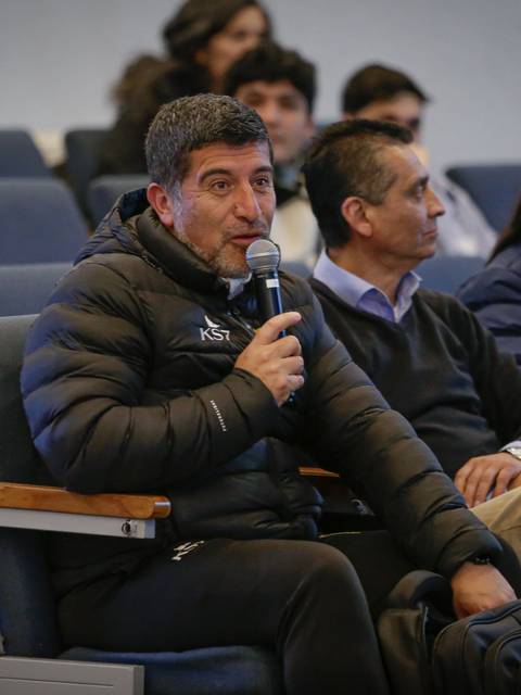 Un hombre habla en una reunión mientras otros participantes lo escuchan atentamente.