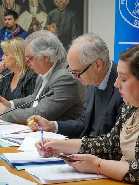 Una reunión en el Senado donde varias personas están discutiendo y tomando notas.