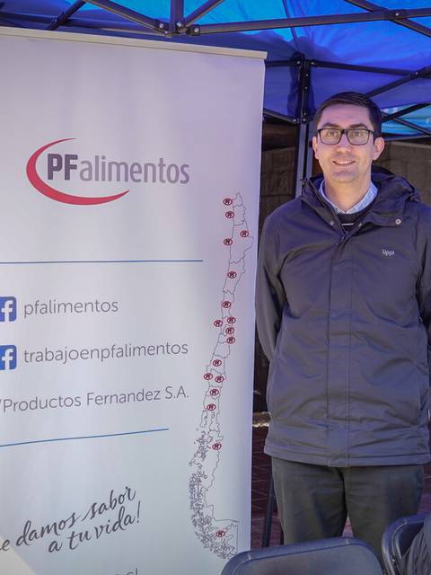 Una persona de pie junto a un banner de la empresa PFalimentos en un entorno al aire libre.