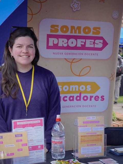 Una mujer sonriente se encuentra frente a un stand de una iniciativa educativa.