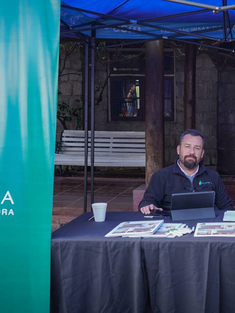 Un hombre está sentado detrás de una mesa en un evento, junto a una pancarta de la constructora La Rioja.