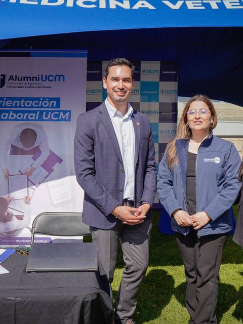 Tres personas posan sonrientes frente a un stand de orientación laboral en un evento universitario.