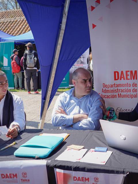 Un grupo de personas interactuando en un evento al aire libre, junto a un stand del DAEM.