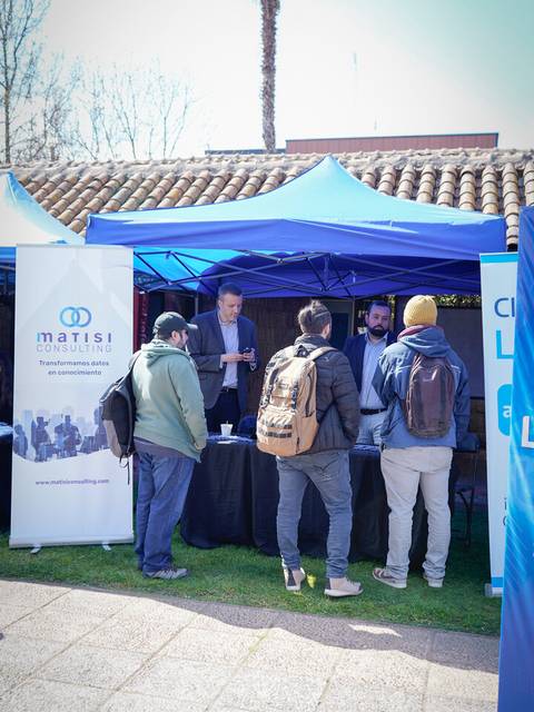 Un grupo de personas conversando en un stand en un evento al aire libre.