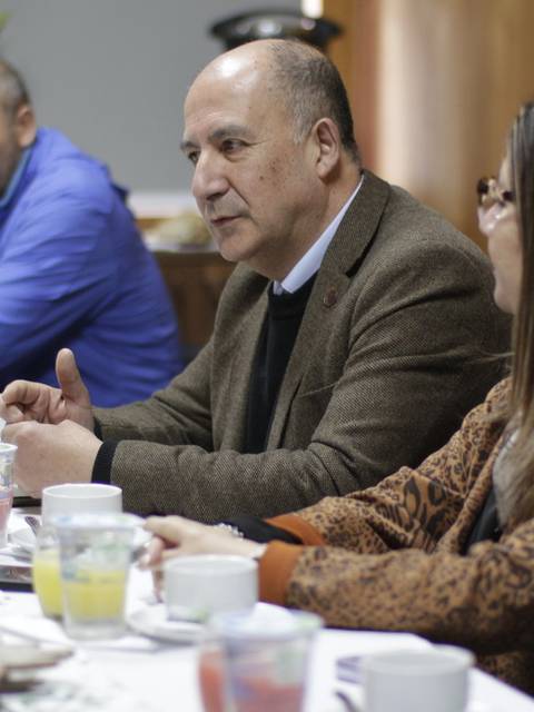 Una reunión informal donde tres personas conversan alrededor de una mesa con comida y bebidas.