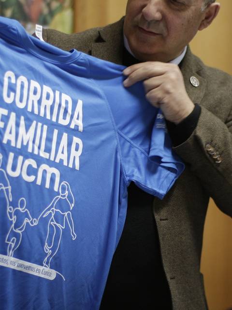 Una persona sostiene una camiseta azul con el texto 'Corrida Familiar UCM'.