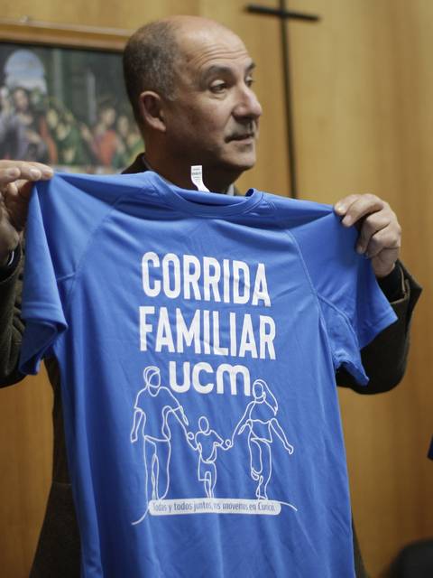 Una persona sostiene una camiseta azul con el texto 'CORRIDA FAMILIAR UCM'.