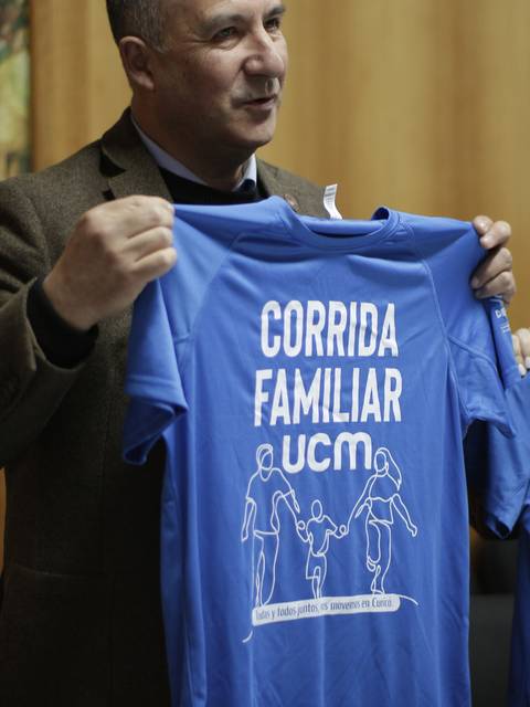 Una persona sostiene una camiseta azul que promueve una corrida familiar organizada por la UCM.