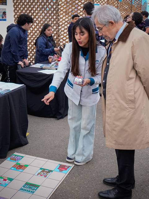 Una mujer explica un juego a un hombre mayor en un evento al aire libre.