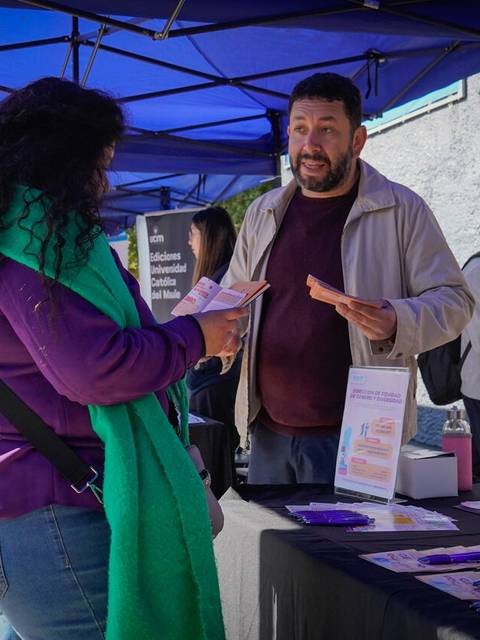 Una mujer interactúa con un hombre en un stand al aire libre bajo carpas azules.