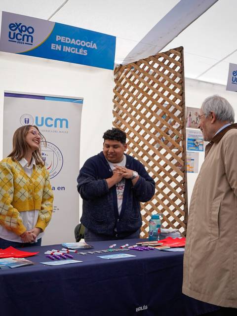 Una feria educativa donde dos personas interactúan en un stand de la UCM sobre pedagogía en inglés.