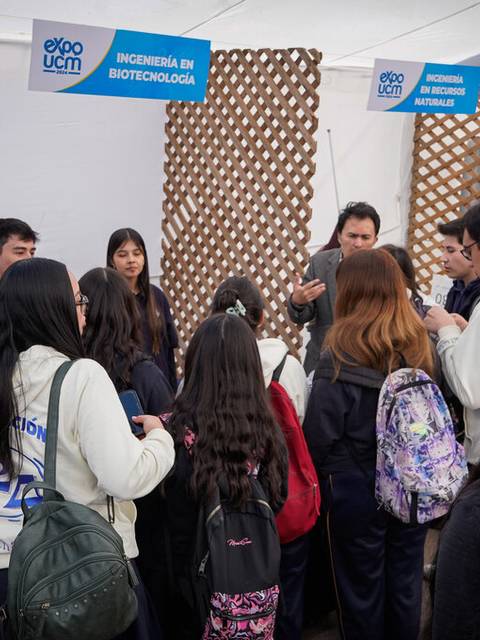 Una feria educativa con varias personas interactuando en un stand de biotecnología.