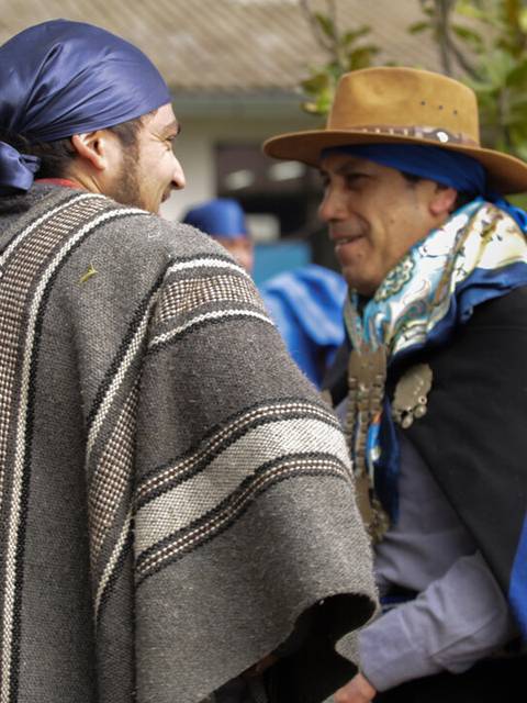 Dos hombres conversan en un evento cultural mientras visten trajes tradicionales.