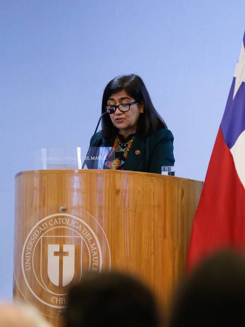 Una mujer habla desde un podio en un evento institucional, con una bandera chilena al fondo.