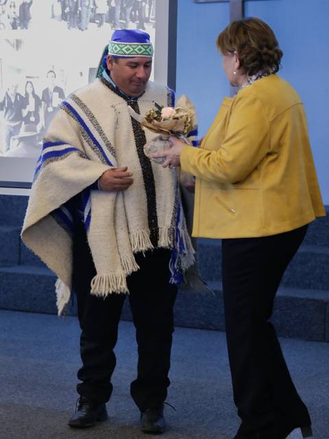 Un hombre vestido con poncho y tocado tradicional recibe un ramo de flores de una mujer en un evento especial.