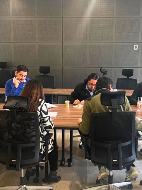 Un grupo de personas está trabajando en una reunión alrededor de una mesa en una sala moderna.