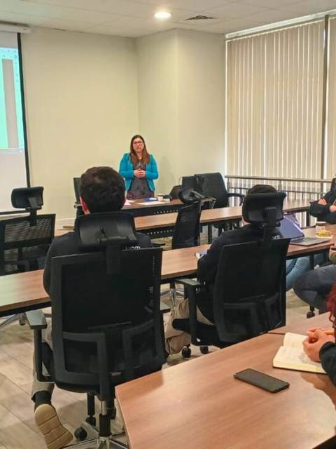 Una presentadora está realizando una charla frente a un grupo de personas en un aula moderna.