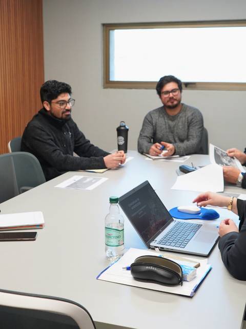 Un grupo de seis personas discute en una sala de reuniones con una mesa rectangular y una laptop sobre la mesa.