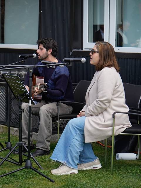 Un dúo musical se presenta en un evento al aire libre con guitarras y micrófonos.