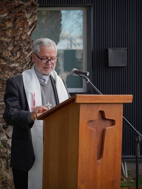 Un hombre vestido de sacerdote está dando un discurso frente a un podio de madera con una cruz en la parte frontal.