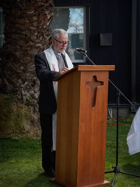 Un hombre está hablando desde un podio de madera en un entorno al aire libre.