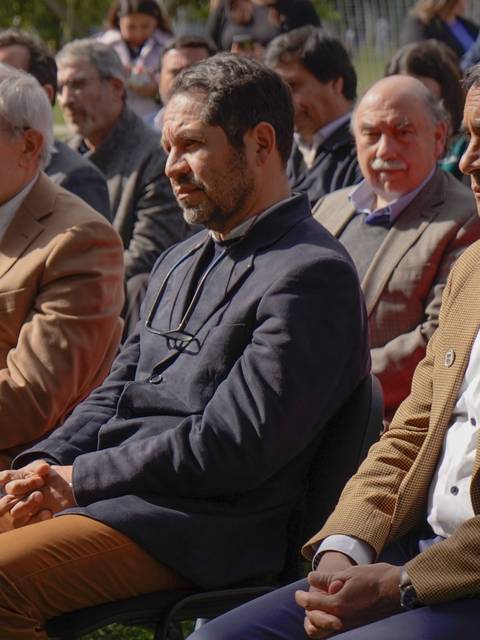 Un grupo de hombres sentados en un evento al aire libre, todos con miradas atentas y serias.