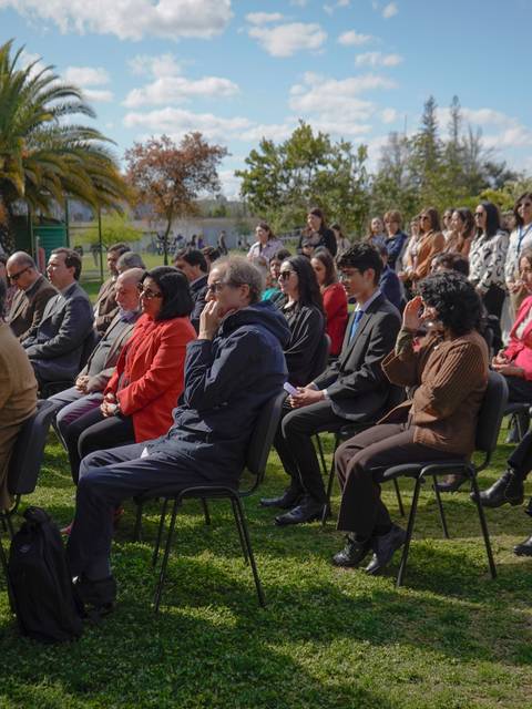 Un grupo de personas sentadas en un evento al aire libre, rodeadas de naturaleza.