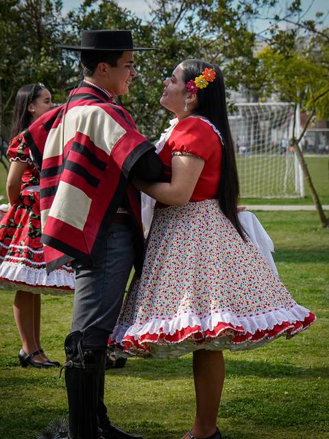Una pareja bailando en un evento festivo, vestidos con trajes típicos y rodeados de un ambiente alegre.