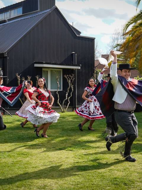 Un grupo de personas bailan vestidas con trajes tradicionales en un jardín al aire libre.