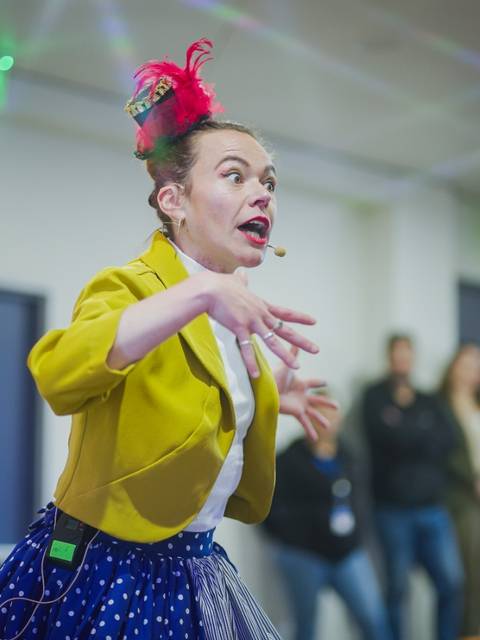Un artista de circo se presenta en un escenario, expresando energía y entusiasmo con un atuendo colorido.