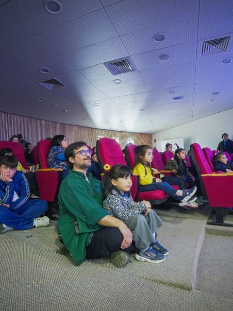 Un grupo de niños y adultos observan una proyección en un cine con asientos rojos.
